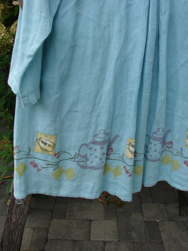 1999 Linen Breeze Jacket Tea & Cherries Spring OSFA draped over a wooden bench, showcasing its light-blue fabric, painted sailor collar, and sweet cherry and teatime motif along the rounded hem.