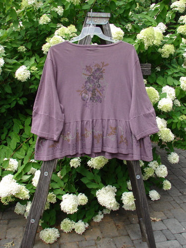 Barclay Peplum Pocket Jacket Magic Garden Dusty Plum Size 2 displayed on a hanger, featuring a full ceramic button front, three-quarter sleeves, and a painted peplum in organic cotton.