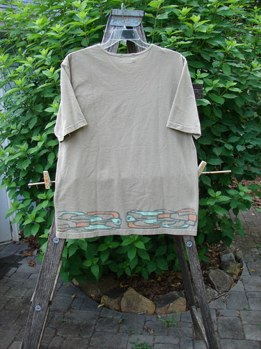Barclay Short Sleeved Tee Stone Path Border Wheat Size 1 displayed on a clothes rack, featuring a rounded neckline, short sleeves, and a straight wide shape with artistic stone path border design.