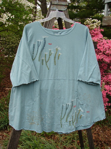 Barclay Three Quarter Sleeved Cafe Pocket Top Fern Blue Tourmaline Size 2, adorned with a floral pattern, featuring a feminine neckline, three-quarter sleeves, and a double side entry kangaroo pocket.