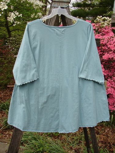 Barclay Three Quarter Sleeved Cafe Pocket Top Fern Blue Tourmaline Size 2 on a wooden rack, showcasing its A-line tunic shape, three-quarter sleeves, and double side entry kangaroo pocket.