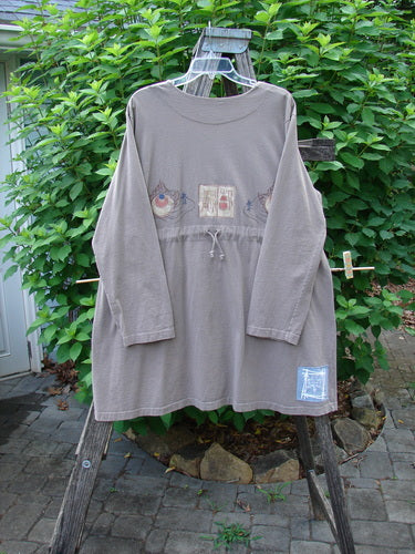1999 Triangle Jacket Far Eastern Shale Size 1 displayed on a wooden post, featuring long sleeves, two oversized painted pockets, a deep V neckline, and a drawcord back with detailed far eastern theme design.