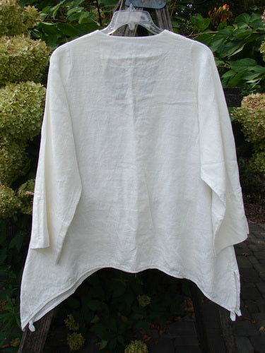 Barclay NWT Linen Basque Cardigan Unpainted White Size 0, displayed on a hanger, features long cuffable sleeves, an asymmetrical hem, oversized shell buttons, and a deep V-neckline against garden foliage.