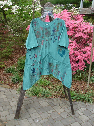 Barclay Three Quarter Sleeved Quad Pocket Tunic Forest Garden Jade Size 2 displayed on a mannequin, showcasing a scooped neckline, wide sleeves, and four drop pockets with a detailed garden theme pattern.