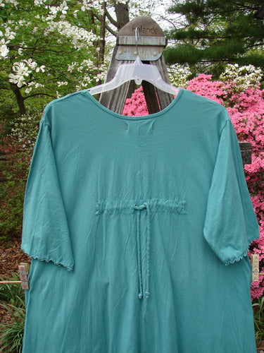 Barclay Three Quarter Sleeved Quad Pocket Tunic Forest Garden Jade Size 2 displayed on a hanger outdoors, showcasing its scooped neckline, widening hem, four drop pockets, and curly three-quarter sleeves.