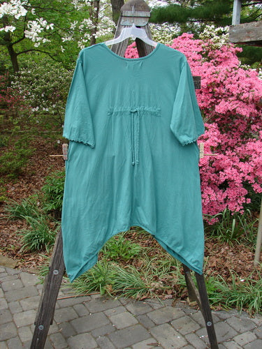 Barclay Three Quarter Sleeved Quad Pocket Tunic Forest Garden Jade Size 2 displayed on a wooden rack, showcasing its rounded scooped neckline, wide three-quarter sleeves, and four drop pockets.