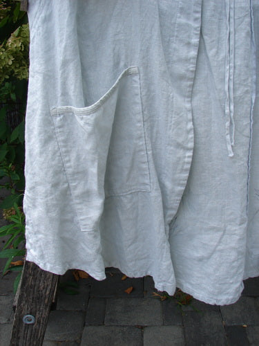 Barclay NWT Linen Contrast Tie Pocket Cardigan Field Twig Dew Size 0 draped over a wooden bench, showcasing its loose fit, roomy patch pocket, visible hem, and tie-strings against a foliage backdrop.