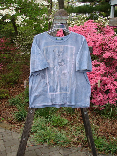 Barclay Short Sleeved Tee Bird Cage Mottled Sky Size 2 displayed on a hanger outdoors, showcasing a rounded neckline, drop shoulders, wide sleeves, and a painted bird cage theme.