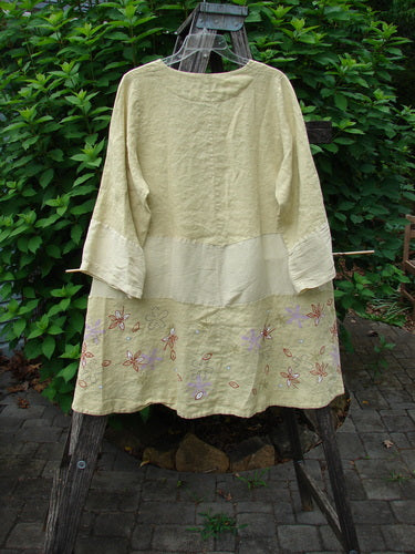 Barclay Linen Wonderland Sectional Banded Cardigan Daisy Chain Celery Size 1, featuring a scooped neckline, belled sleeves, thick pearly buttons, and unique horizontal panels with a whimsical daisy chain design.