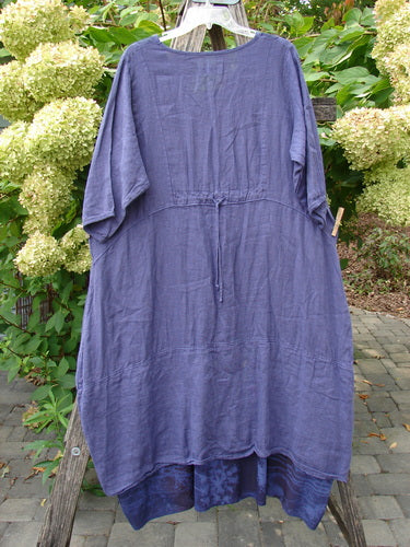 Barclay NWT Linen Process Two Story Dress Mum Ultra Violet Size 0, showcasing a loose-fitting, long-sleeved, ankle-length silhouette in lightweight linen, displayed outdoors on a hanger with hydrangea blooms in the background.