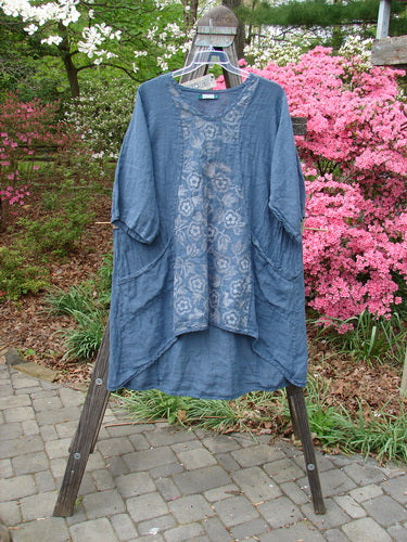 Barclay NWT Linen Posey Tunic Buttercup Patch Blue Echo Size 2 displayed on a hanger outdoors, showcasing its slight oval neckline, three-quarter sleeves, and oversized slant pockets.