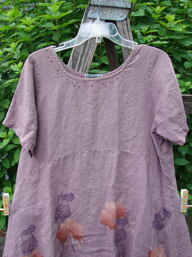 Barclay Linen Urchin Dress Necklace Leaf Dusty Plum Size 0 showcased outdoors, featuring a painted hemline and slight reverse bell shape, with a continuous tiny floral necklace pattern over medium weight linen.