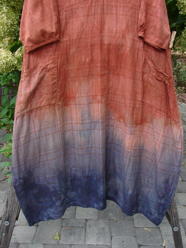 Barclay NWT Flannel Cross Over Blue Moon Pocket Dress Terra Ombre Plaid Size 0 hangs on a wooden bench outdoors, showcasing its ombré design from rusty red to deep indigo.