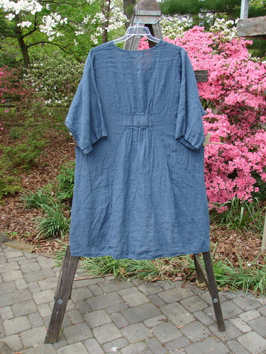 Barclay NWT Linen Posey Tunic Buttercup Patch Blue Echo Size 2 displayed on a wooden stand, showcasing its slight oval neckline, oversized billowy pockets, and three-quarter length sleeves.