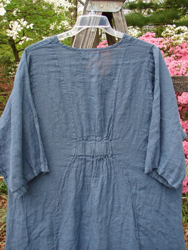 Barclay NWT Linen Posey Tunic Buttercup Patch Blue Echo Size 2 hanging on a wooden fence, showcasing its flowy design, oval neckline, oversized slant pockets, and three-quarter sleeves.