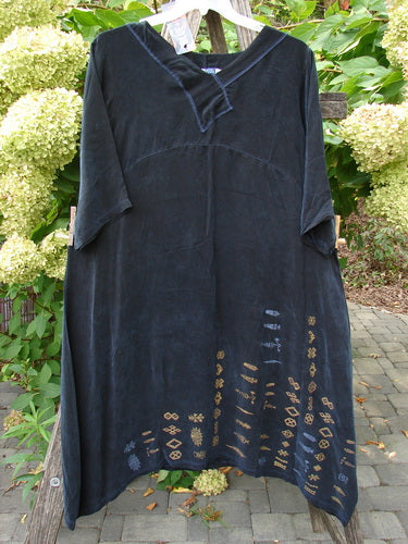 Barclay NWT Cupro Cross Over Urchin Dress, a knee-length black tunic with a V-neck, embroidered hem, and short sleeves, hanging on a rustic frame. Made from lightweight Cupro for an elegant evening look.