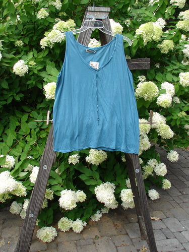 Barclay NWT Batiste Decora Tiny Tank Unpainted Peacock Size 2 hangs on a wooden ladder, showcasing its delicate front vertical neckline tie and gather, and slight A-line shape.
