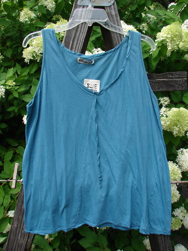 A blue tank top on a wooden stand, part of the Barclay NWT Batiste Decora Tiny Tank collection in Peacock. Made from featherweight cotton batiste, it features a shorter A-line shape, a front vertical neckline tie and gather, and a diagonal insert. Size 2, unpainted.