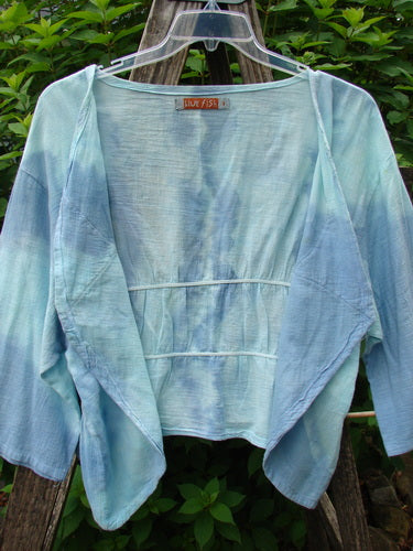 Barclay Gauze Open Front Shrug Mottled Sky Size 1 displayed on a rack, featuring a fully open front, three-quarter sleeves, and a flounce-enhancing dual elastic gathering.