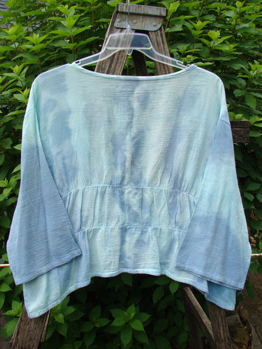 Barclay Gauze Open Front Shrug in Mottled Sky displayed on a hanger, showcasing its reverse triangular upper panels, three-quarter sleeves, and flowing hemline with dual horizontal elastic gatherings.