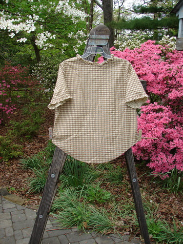 1996 Woven Boardwalk Top Unpainted Gingham White Pine Size 2 displayed on a wooden easel outdoors, showcasing unreal gathered ruffle neck and sleeve lines, rounded hem, and bust line darts.