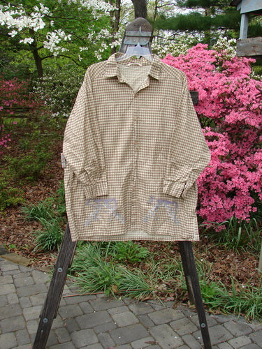1996 Woven Tourist Top Farm Cow White Pine Gingham OSFA displayed on a hanger, featuring wooden buttons, rollable sleeves, vented sides, and a farm cow border theme, reflecting a classic country work shirt style.