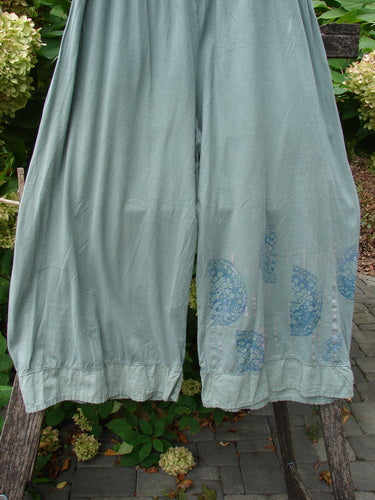 Barclay Flutter Bottom Crop Cargo Pant Medallion Vine Size 0, featuring wide legs, elastic waist, and circular block-print near the hem, displayed outdoors on a wooden frame amidst garden plants.