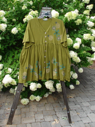 Barclay Tree Top Cardigan Dress in Olive with floral blossom design, featuring a baby doll style, V-neckline, pearly buttons, and gathered lower section, displayed hanging outdoors.