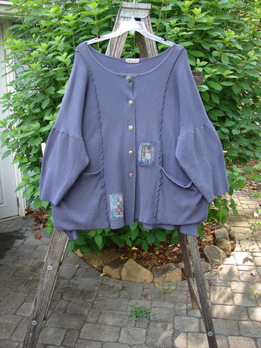 Barclay Patched Thermal Curl Pocket Cardigan Geos Royal Orchid Size 3 displayed on a wooden rack, showcasing its full button front, dolman sleeves, and drop front pockets with geometric patchwork details.