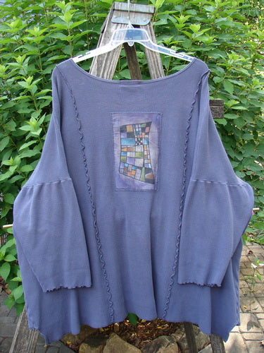 Barclay Patched Thermal Curl Pocket Cardigan Geos Royal Orchid Size 3: A close-up view of a blue cardigan with a patchwork design, featuring button front, dolman sleeves, and vertical curved stitchery.