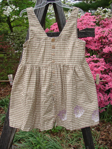 1996 Woven Roadside Jumper Flower Wheel White Pine Gingham Size 1 on a wooden stand, featuring wooden buttons, pleated shape, squared neckline, and floral paint, displayed outdoors against pink flowers.
