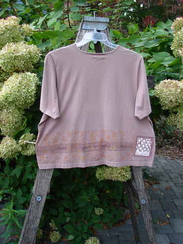 2000 Short Sleeved Crop Tee Floral Fence Border Coralline Size 2, featuring a boxy cut, decorative hem band, and signature Blue Fish patch, displayed on a ladder against a lush garden backdrop.