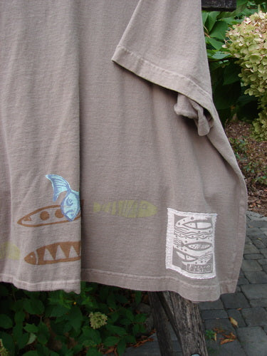 1999 Tiny Pocket Top Fishie Riverbed Size 2 features a taupe short-sleeved design with stenciled fish motifs along the hem, draped outdoors over a wooden rail, highlighting its playful, vintage aesthetic.