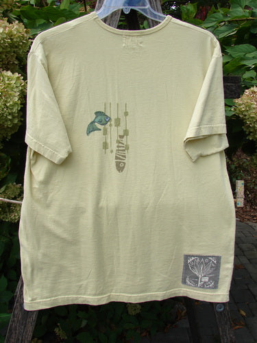 1999 Short Sleeved Tee Single Fish Citron Size 1, featuring a blue fish graphic and abstract shapes, draped on a trellis with plants. Organic cotton, boxed shape, and signature Blue Fish patch.