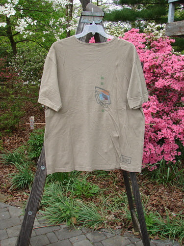 2000 Artist Choice Short Sleeved Tee Geo Dove Size 1 displayed on a wooden hanger, showcasing its drop shoulders, rolled and ribbed neckline, and generous shape with simplistic geometric designs.