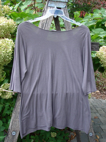 Barclay Batiste Raw Edge Layering Tee Unpainted Pebble Size 1 features a loose fit, three-quarter sleeves, and a raw-cut neckline, displayed on a hanger against a natural backdrop.