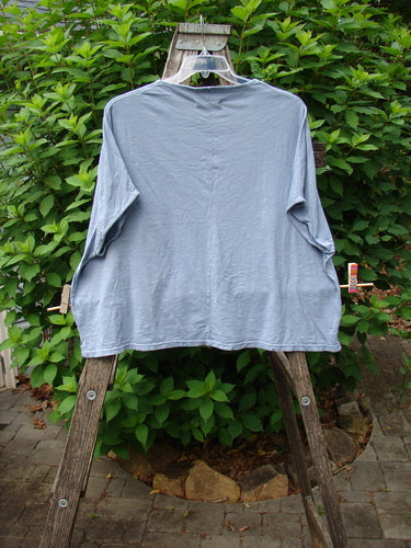 Barclay Cotton Slub Cricket Cap Sleeve Tee Sun Guy Dusty Blue OSFA displayed on a wooden rack, showcasing its cap sleeves, seamless shoulder design, and rounded hemline, embodying Bluefishfinder.com's unique vintage style.
