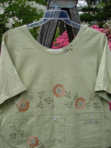 1996 Collector's Top Floral Seedling Size 2 featuring a green shirt adorned with a floral pattern, wider painted neckline, A-line flare, and multiple pockets with tiny paper buttons for a vintage spring look.