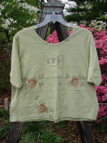 1996 Collector's Top Floral Seedling Size 2 featuring a green shirt adorned with a floral pattern, wider neckline, slight A-line flare, multiple pockets, and tiny paper buttons for a vintage touch.