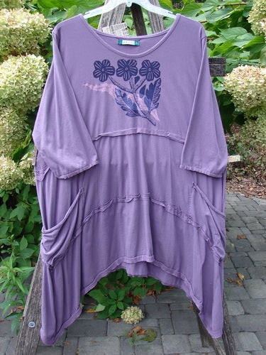 Barclay NWT Raw Seam Vector Tunic Dress in Tri Floral Violet Size 2, features a loose fit, three-quarter sleeves, draped side pockets, and floral print, hanging outdoors on a clear hanger.