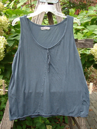 Barclay Batiste Decora Tiny Tank in Unpainted Navy, Size 2, displayed on a hanger. Features a loose-fit, sleeveless design with vertical neckline ties and diagonal inserts, against leafy garden foliage.