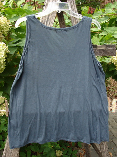 Barclay Batiste Decora Tiny Tank Unpainted Navy Size 2 displayed on a clear hanger against a lush outdoor backdrop, showcasing its sleeveless design, vertical neckline tie, and diagonal insert for versatile styling.