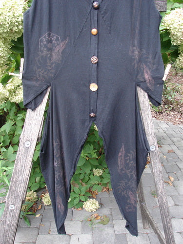 Barclay Calligrapher's Vest Asian Inspiration Black Size 0, featuring mismatched buttons, three-quarter sleeves, and a jagged hem, hung on a ladder outdoors amidst paving stones and shrubs.