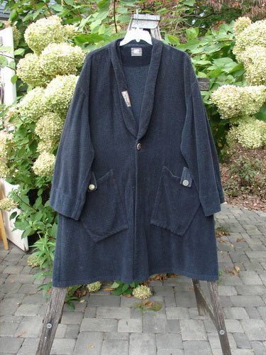 1999 Patched Chenille Angle Pocket Jacket Holiday Black Size 1 hangs on a wooden stepladder, showcasing its shawl collar, central button closure, oversized angled pockets with buttons, and full-length sleeves.