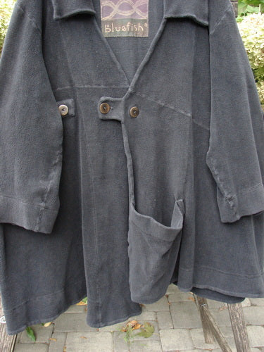 2000 Celtic Moss Highlander Coat Unpainted Black Size 1, featuring oversized patch pockets, two front buttons, and a bluefish label, hanging outdoors over a chair, showcasing its heavy-knit fabric and unique design.
