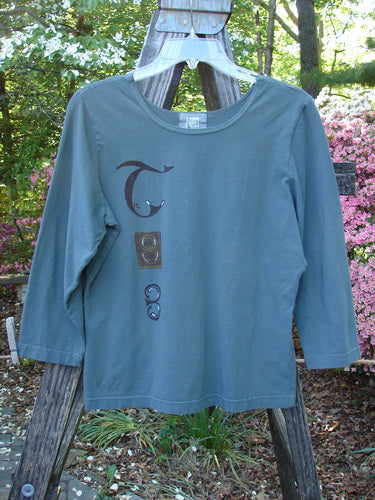 2000 Cotton Lycra Three Quarter Sleeve Layering Top Celtic Park Size 0 displayed on a hanger outdoors, showcasing its forgiving stretch fabric and vertical Celtic theme paint.