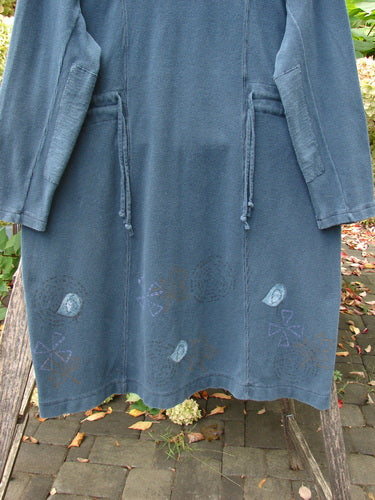 1999 Thermal Home Dress Paisley Peacock Size 0, featuring a teal-blue tunic-style jacket with patch pockets, drawstring waist, and spiral motifs, draped outdoors over a bench amidst a brick-paved surface.