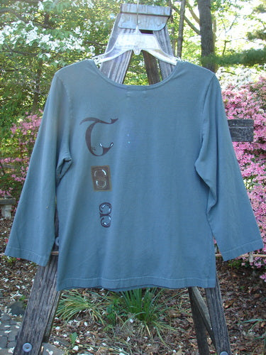 2000 Cotton Lycra Three Quarter Sleeve Layering Top Celtic Park Size 0 displayed on a wooden hanger outdoors, featuring vertical Celtic theme paint and super stretch fabric for easy layering.