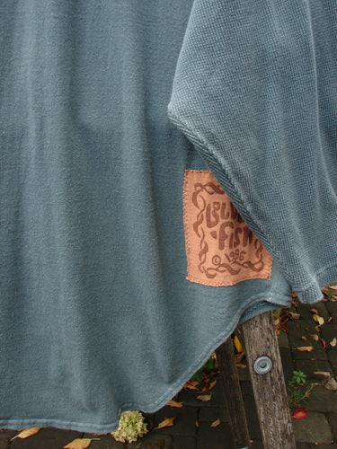 The 1996 Celtic Filias Jacket, draped on a ladder, showcases its teal-blue waffle-knit texture with a leather patch. Ideal for expressing individuality, it's part of Blue Fish's vintage collection.