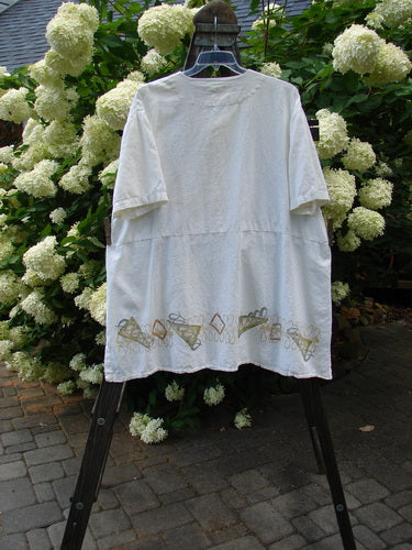 2000 Hemp Viscose Asymmetric Top Space White Size 1 displayed on a hanger, showcasing its button front, V-shaped neckline, side-vented hem, and lower drop pocket with floral embroidery.